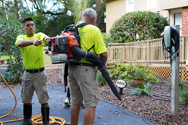technician starts a leaf blower as another technician stands by